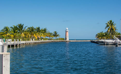 Lighthouse by sea against clear blue sky