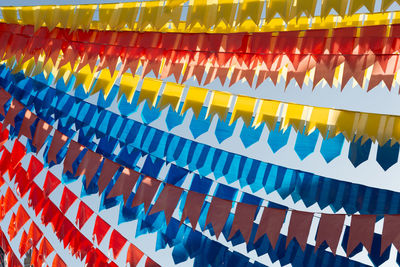 Colorful plastic flags hang with string between houses for parties against the blue sky.