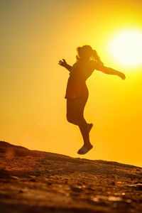 Silhouette woman with arms raised standing against sky during sunset