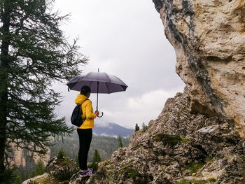 Rear view of man with umbrella walking on rock