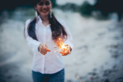 Cheerful woman holding lit sparklers at lakeshore
