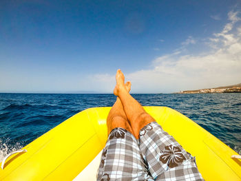 Low section of man relaxing on pool raft over sea against sky