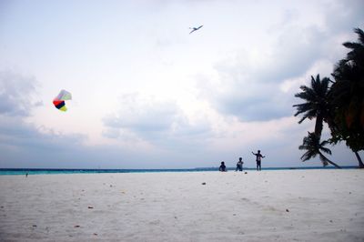 Children flying kite against sky at beach