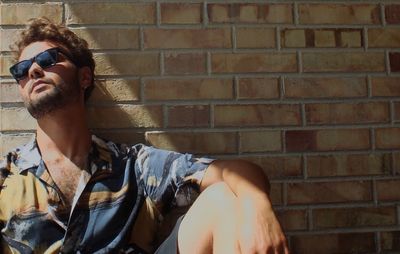 Portrait of young man sitting against wall