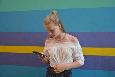 Teenage girl using phone while standing against colorful wall