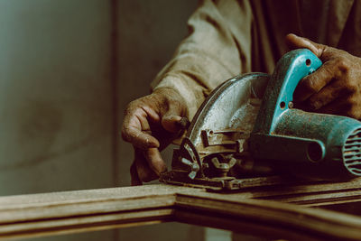 Midsection of carpenter cutting wood with circular saw in workshop