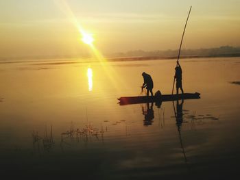 Silhouette men fishing in lake against sky during sunset