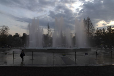 Fountain in city against cloudy sky