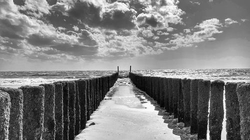 Wooden posts on footpath by sea against sky