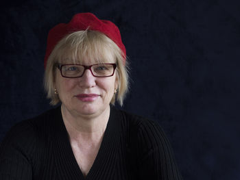 Portrait of smiling mature woman with red cap against black background