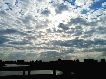 Silhouette bridge over river against sky in city