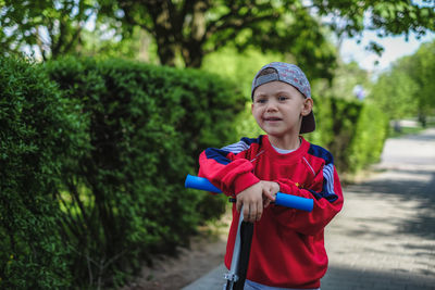 Cute boy with push scooter looking away while standing in park