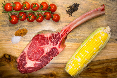 Wagyu tomahawk steak on wooden board with tomatoes and corn