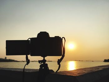 Close-up of silhouette camera against sea during sunset