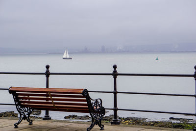 Bench by sea against sky during winter