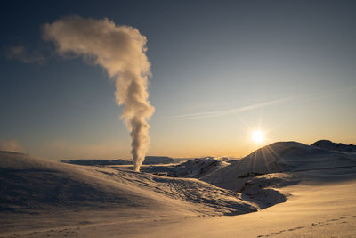 Smoke emitting from snowcapped mountain against sky during sunset