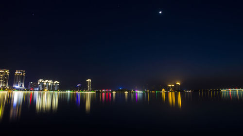 Illuminated city by sea against sky at night