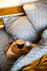 Coffee in a modern cup with a double bottom on a tray with creamer in bed with blue textured linen.