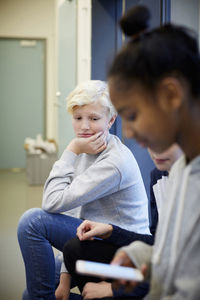 Bored middle school boy sitting with friends in corridor