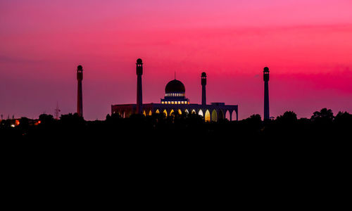 Silhouette factory against sky during sunset