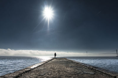 Distance view of person standing on pier over sea against sky