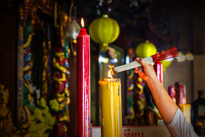 Cropped hand of person lighting incense sticks at temple