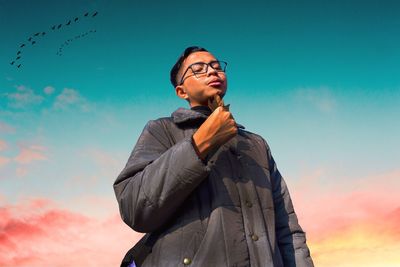 Low angle view of young man standing against sky during sunset