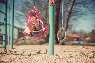 Full length of playful girl wearing warm clothing while swinging at playground