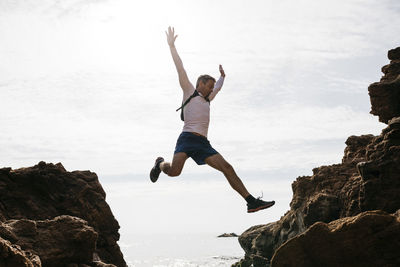 Full length of woman jumping on rock against sky