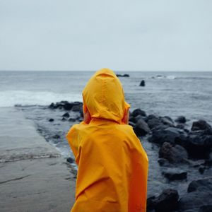 Rear view of boy in yellow raincoat standing on beach
