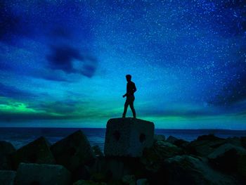 Silhouette man standing on rock by sea against sky