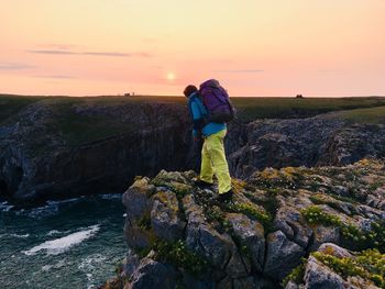 Man standing on rock against sky during sunset