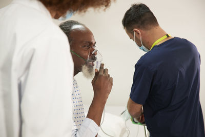 Patient wearing oxygen mask with healthcare workers in medical room