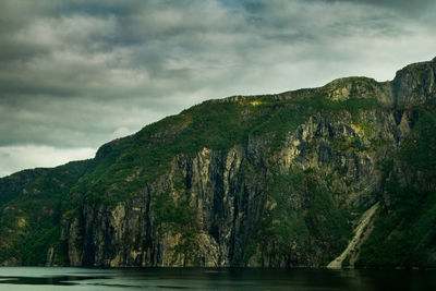 Scenic view of sea by mountain against sky