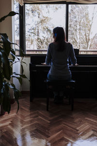 Rear view of young woman playing piano