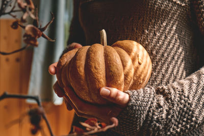 Female in knitted brown woolen sweater holding orange pumpkin. cozy autumn vibes. fall mood.