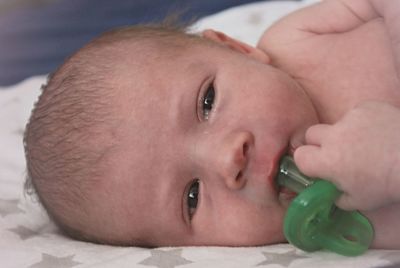 Close-up portrait of cute baby boy holding pacifier while lying on bed