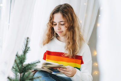 Beautiful teenager girl reading book sitting on windowsill in the cozy children room