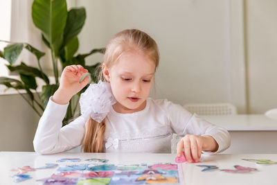 A girl student sits at a desk in the classroom and collects figures / puzzles / small toys 