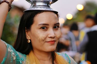 Portrait of smiling woman with face paint carrying containers on head during event