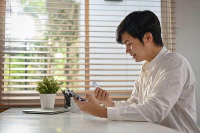 Side view of young man using mobile phone while sitting on table