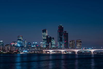 Illuminated buildings by river against sky in city at night