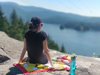 Woman sitting on shore by lake against mountains