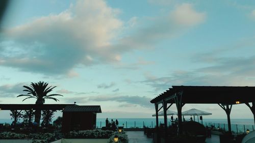 Palm trees by sea against cloudy sky