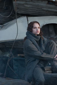 Thoughtful young woman sitting on tire at junkyard