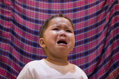 Close-up of boy crying against curtain