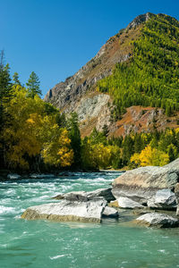 Scenic view of waterfall in mountains against clear blue sky