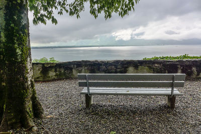 Empty bench by sea against sky