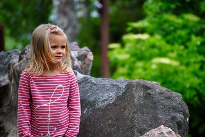 Cute girl looking away while standing by rock