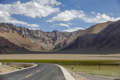 A flat, newly built wide asphalt road leads to the beautiful mountains in the distance